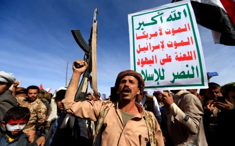 Un miliziano Houthi con le bandiere dello Yemen e del movimento armato ribello (con slogan in arabo).