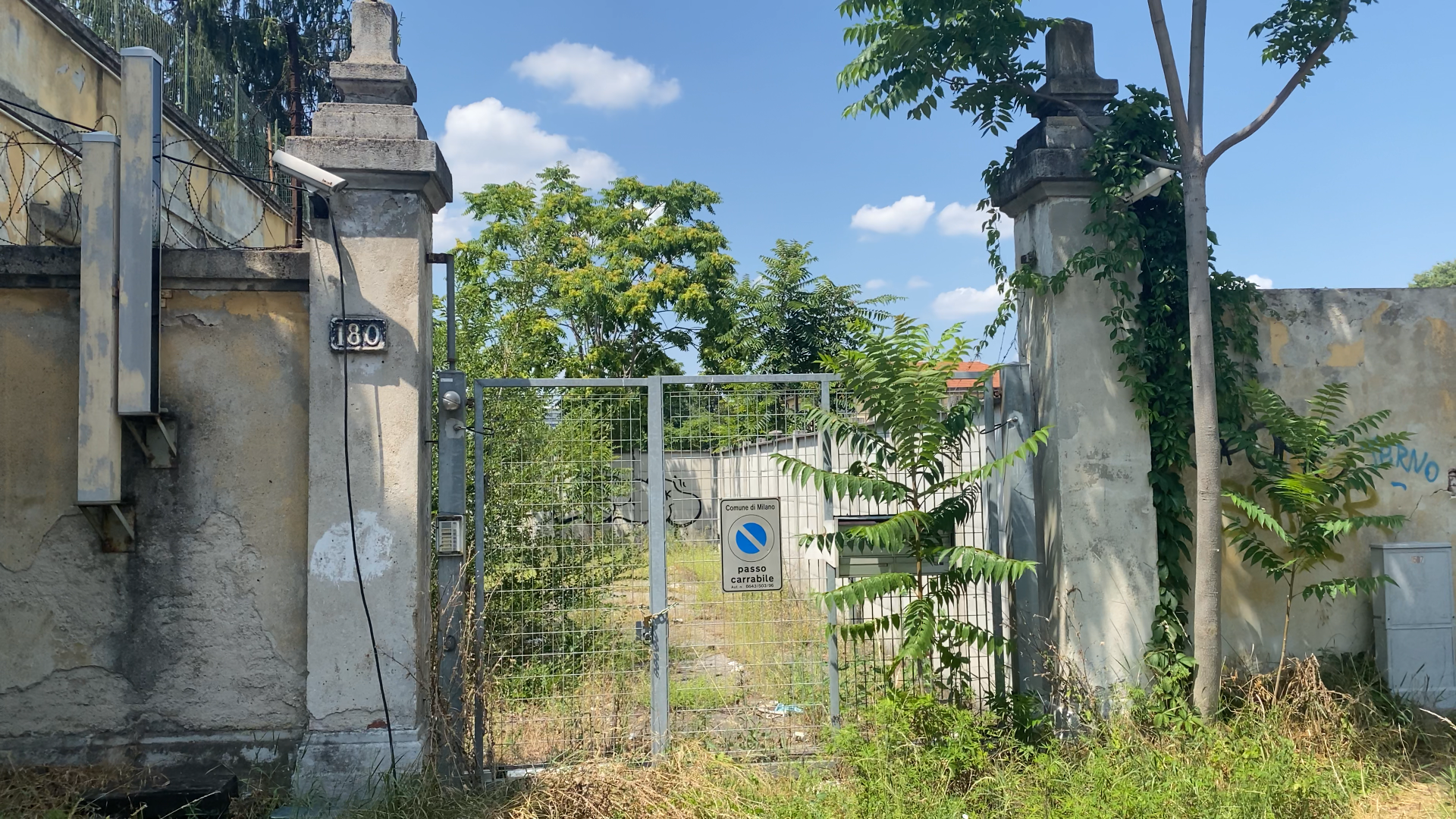 Il cancello dell'edificio su Via delle Forze Armate nel luglio 2023. Dal cancello, non coperto, si vede il muro perimetrale ancora intatto.