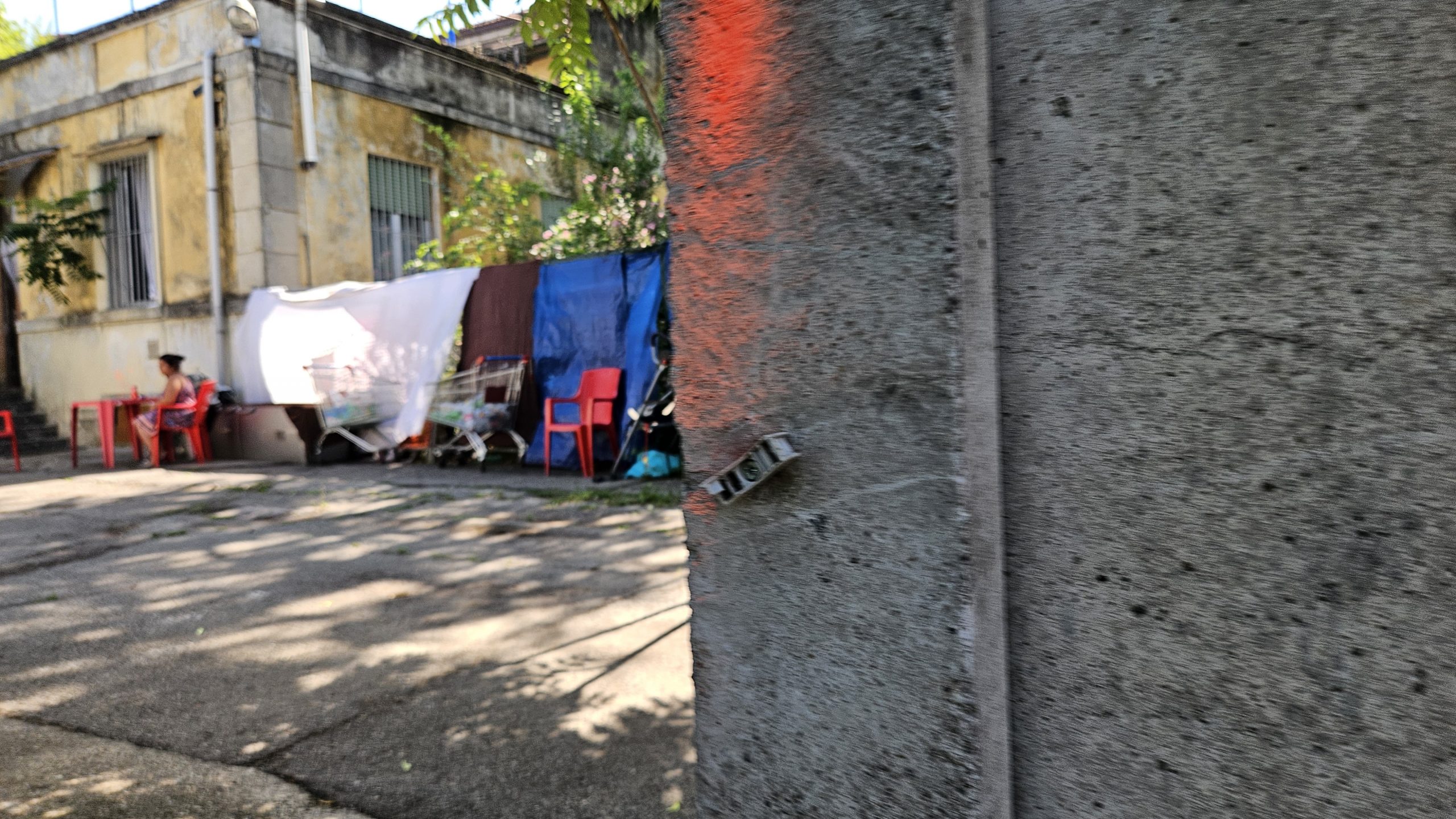 Attraverso un varco nel muro di cinta, che un anno fa non c'era, si accede alla palazzina occupata. Fuori, un cortiletto con tavoli e panni stesi.