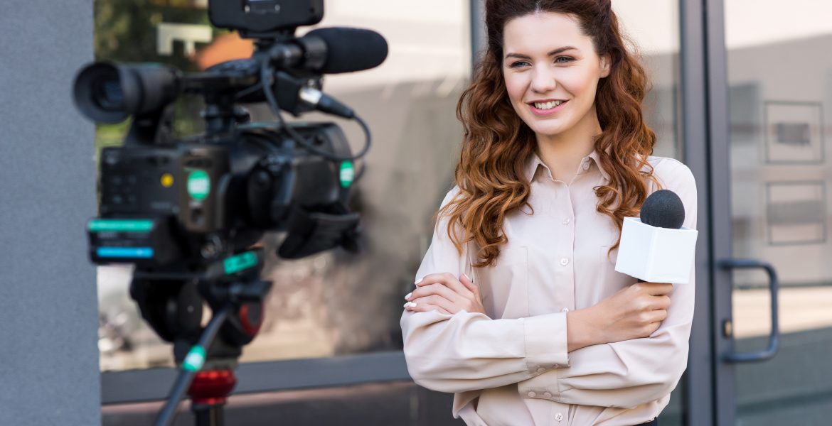 smiling journalist with microphone standing in front of digital video camera