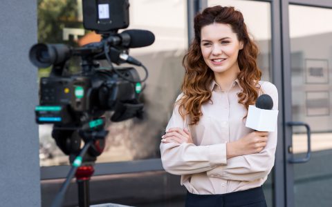 smiling journalist with microphone standing in front of digital video camera