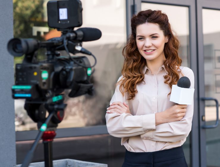 smiling journalist with microphone standing in front of digital video camera