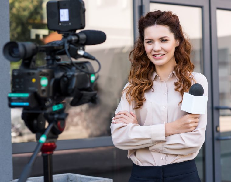 smiling journalist with microphone standing in front of digital video camera