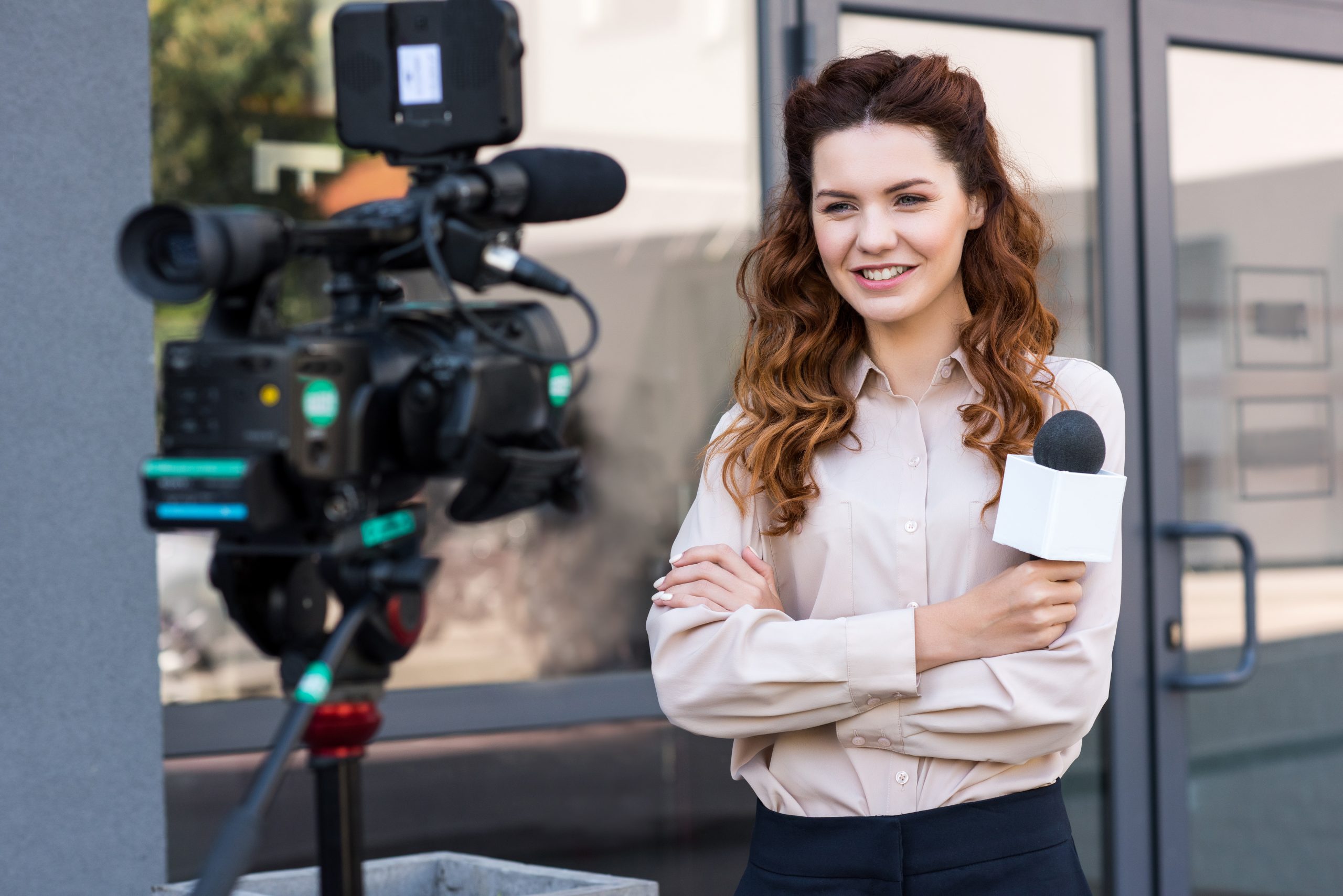 smiling journalist with microphone standing in front of digital video camera